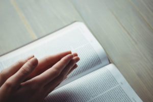 hands praying over open Bible