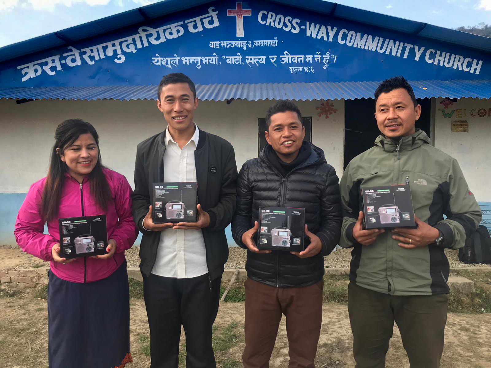 Four Nepali people standing outside church holding radios