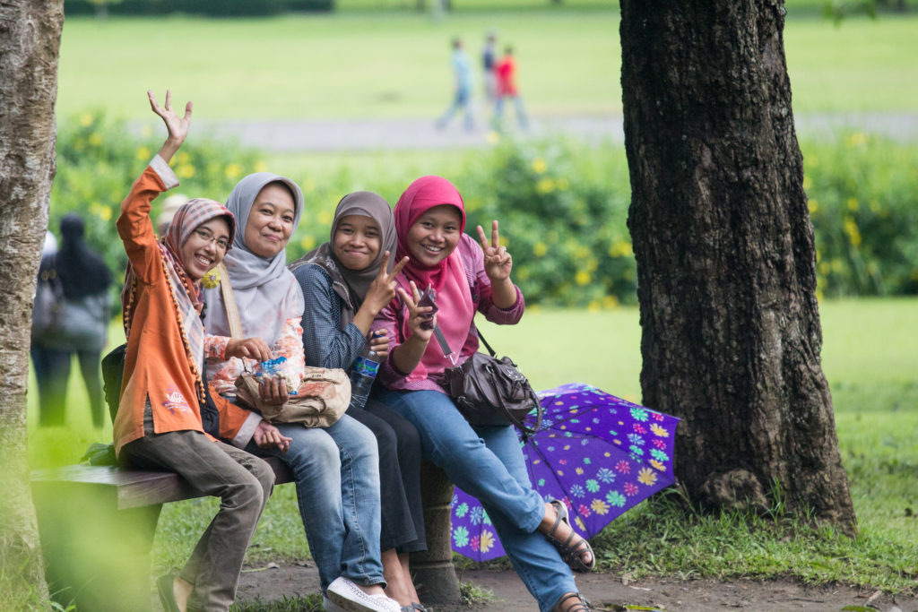 Four Muslim women sitting on park bench happy waving